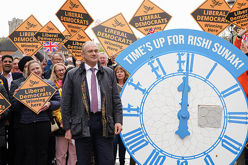 Ed Davey in front of crowd with Lib Dem diamond signs and clock with words time's up for Rishi Sunak