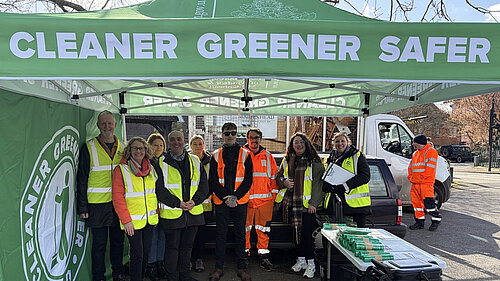Group of people standing under a gazebo with cleaner, greener, safer on it